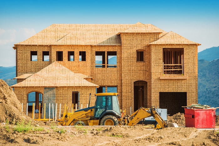 House in the framing stages with a backhoe sitting in front.