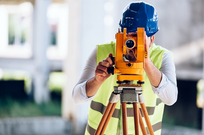 Construction worker looking through the lens of a transit used for surveying lot lines, building corners, etc.