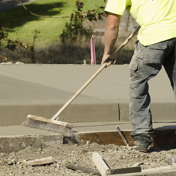 Man putting a broom finish on a sidewalk patch of concrete.